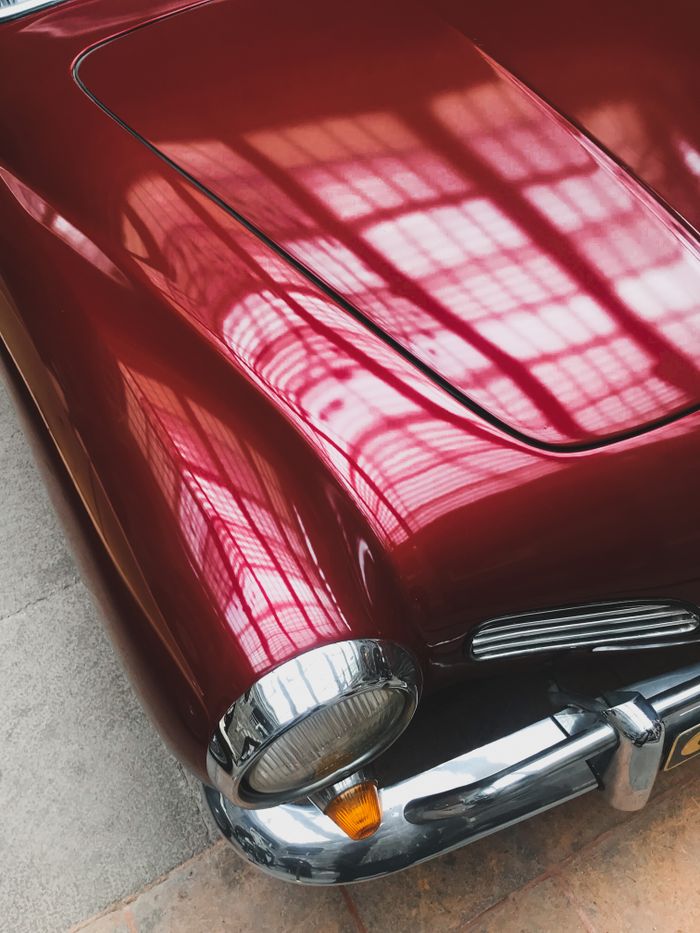 Close-up of a shiny red vintage car hood reflecting intricate window patterns.